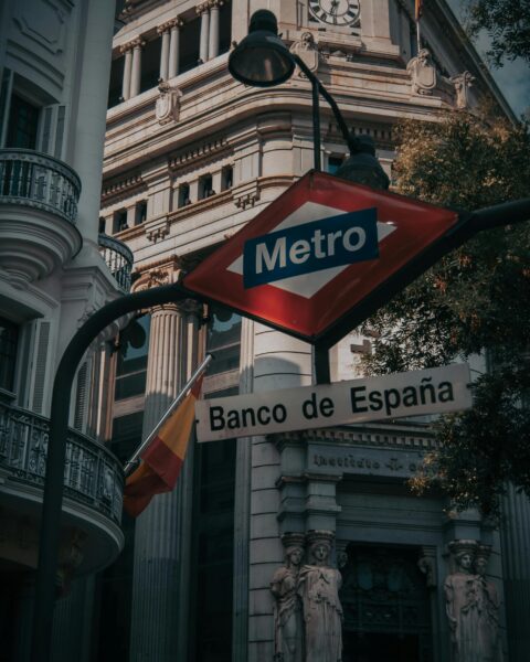 Urban view of Madrid's Banco de España with metro sign in the foreground, capturing city life.